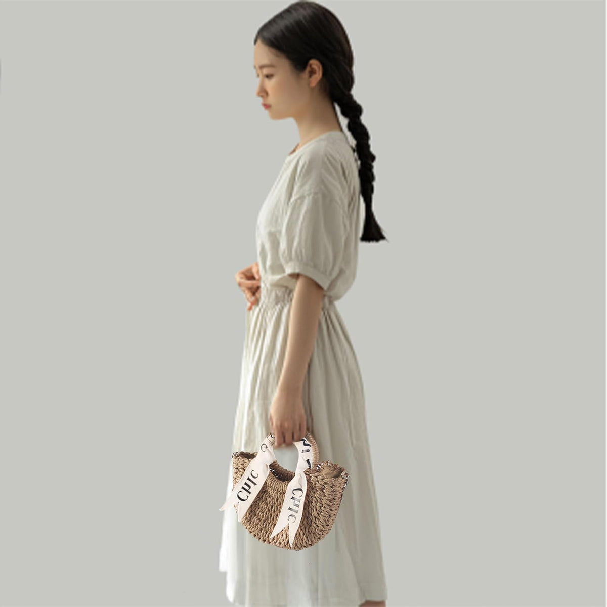 Eiyye Off White Burlap Woven Straw Shoulder Bag Held by Hand Highlighting Elegant Shape and Lightweight Design